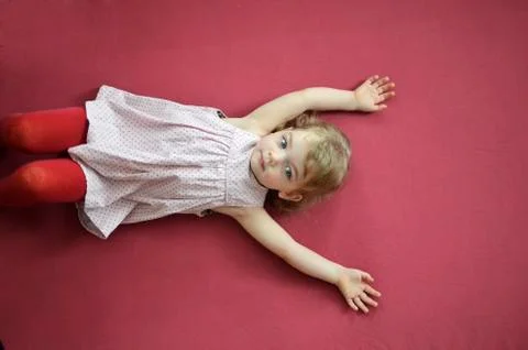 Little blonde lying on a dark pink background. Stock Photos