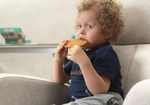 Little boy 3 years old in chair watching cartoon in room and eating biscuits Foto stock
