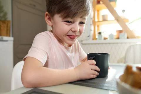A little boy of 7 years in the kitchen drinks tea from a gray cup. Stock Photos