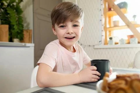 A little boy of 7 years in the kitchen drinks tea from a gray cup. Stock Photos