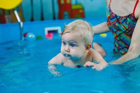 A little boy of 9 months is learning to swim in the pool with a coach. Stock Photos