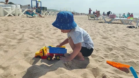 A little boy aged 2 years old in a Panama hat plays with toys and sand on the Stockbeeldmateriaal 296226841
