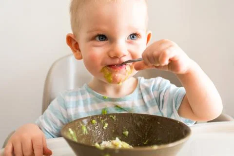 Little boy alone eats puree from a plate. Stock Photos