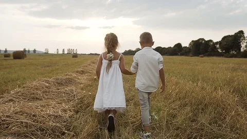 Little boy and girl after the rain took hands handsome running on the field Stock Footage