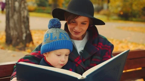Little boy and his mother are watching family album in the autumn park Stock Footage 82887953