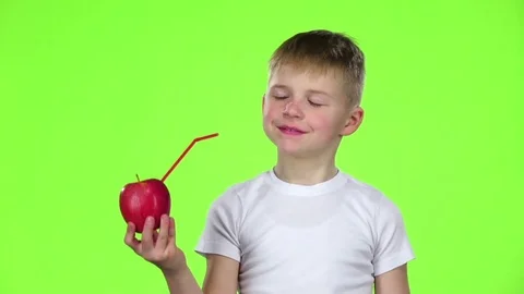 Little boy is an apple with a straw and drinks juice from it. Green screen. Slow Stock Footage 75792995