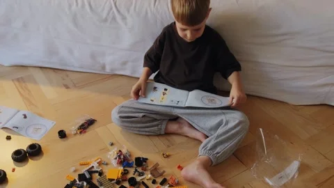 A little boy assembles a construction set while sitting on the floor. Stock Footage 252382326
