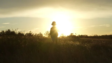 Little boy with backpack walking into sunset across steppe Stock Footage 317334864