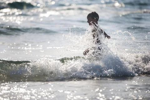 A little boy on the beach, playing with the waves Stock Photos