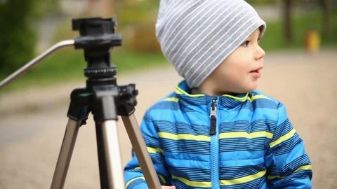 Little boy being curious while touching camera tripod in the park Stock Footage 75216031