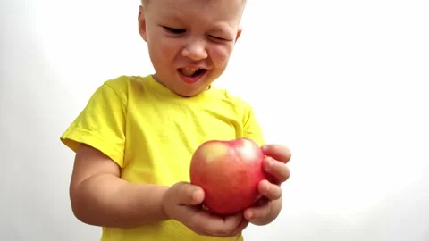 Little boy bites red apple on white background in yellow T-shirt close-up Stock Footage 234571540