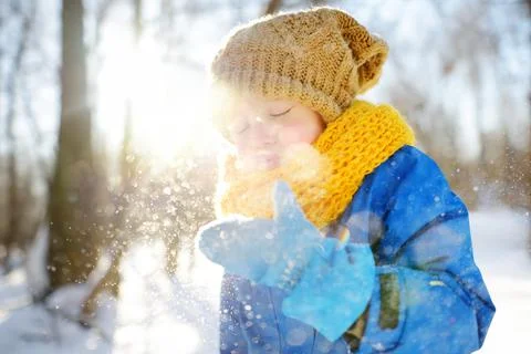 Little boy blowing snow from his hands. Child enjoy walking in the park Stock Photos