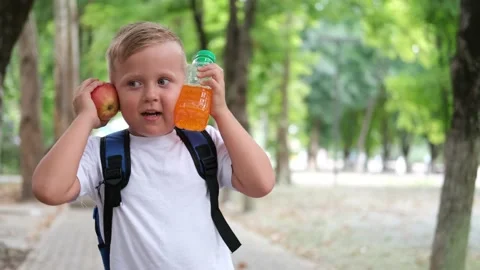 A little boy with a briefcase on his back eats an apple. Stock Footage 208336279