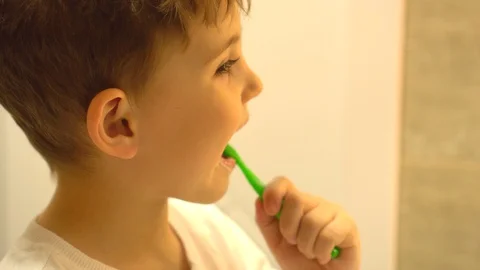 A little boy brushes his teeth in the bathroom with a green toothbrush Stock Footage 128778481