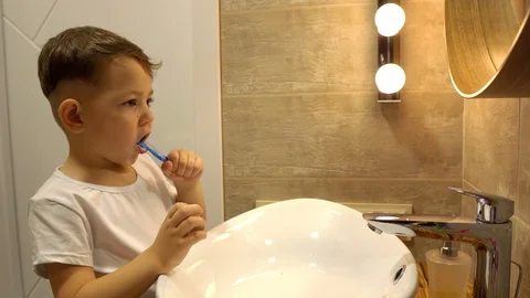Little boy brushing his teeth in a home bathroom, looking at his own reflection Video stock 128779597