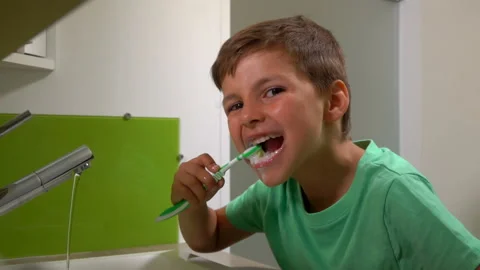 Little boy is brushing his teeth in the bathroom looking at the camera Stock Footage 212574968