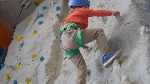 Little boy climbing a rock wall in a harness indoor. Concept of sport life. Stock Footage 106840256