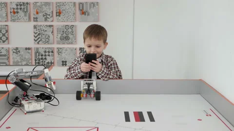 Little boy controls a robot using his phone in a robotics class. Stock Footage 153154429