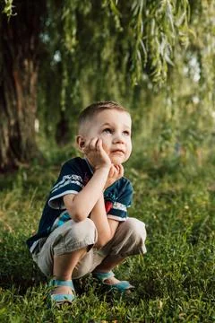 A little boy crouched under a tree, his hand propping up his head and angry Stock Photos