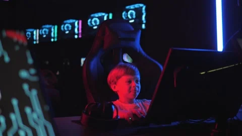 A little boy in a dark computer club with lots of computers is playing a game. Stock Footage 331696535