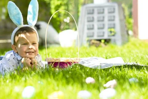 A little boy with the decorative ears of an Easter bunny lies on the lawn. Stock Photos