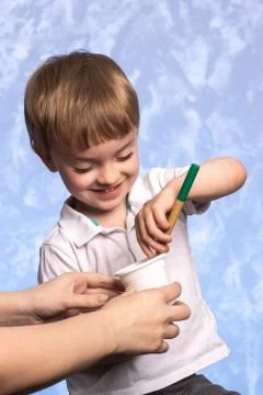 A little boy dips a bamboo toothbrush into a biodegradable cornstarch cup. Stock Photos