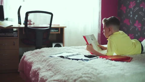 Little boy does homework, reads a book in bed. books are scattered on the bed. Video stock 132034763