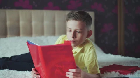 Little boy does homework, reads a book in bed. books are scattered on the bed. Video stock 132034885