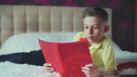 Little boy does homework, reads a book in bed. books are scattered on the bed. Video stock 132034940