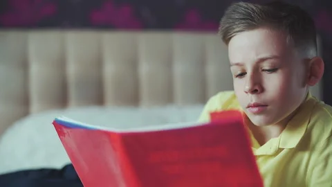 Little boy does homework, reads a book in bed. books are scattered on the bed. Video stock 132035032