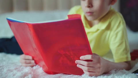 Little boy does homework, reads a book in bed. books are scattered on the bed. Video stock 132035148