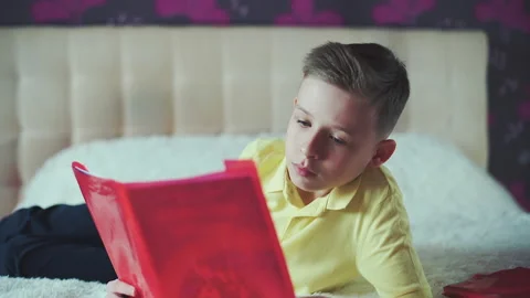 Little boy does homework, reads a book in bed. books are scattered on the bed. Stock Footage 132035185