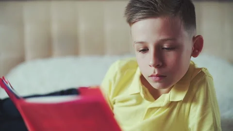 Little boy does homework, reads a book in bed. books are scattered on the bed. Video stock 132035283
