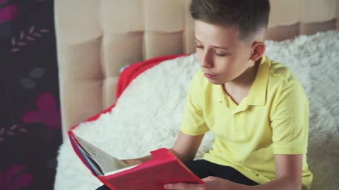 Little boy does homework, reads a book in bed. Books are scattered on the bed, Video stock 132035443
