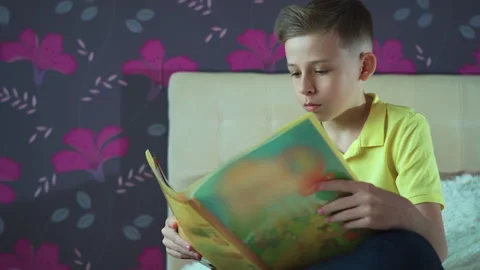 Little boy does homework, reads a book in bed. Books are scattered on the bed, Video stock 132035642
