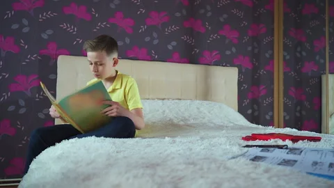 Little boy does homework, reads a book in bed. Books are scattered on the bed, Video stock 132035837