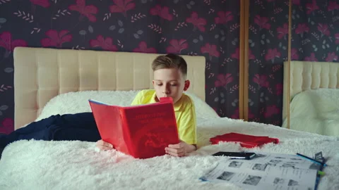Little boy does homework, reads a book in bed. books are scattered on the bed. Stock Footage 132057891