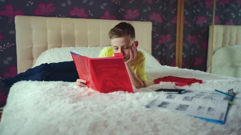 Little boy does homework, reads a book in bed. books are scattered on the bed. Stock Footage 132058228