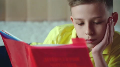 Little boy does homework, reads a book in bed. books are scattered on the bed. Stock Footage 132058447