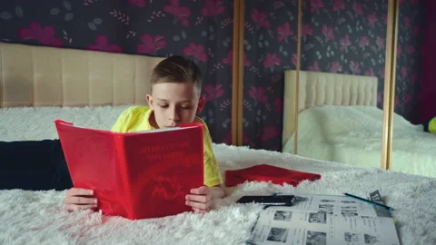Little boy does homework, reads a book in bed. books are scattered on the bed. Stock Footage 132058629