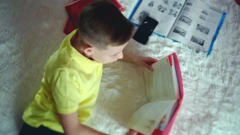 Little boy does homework, reads a book in bed. books are scattered on the bed. Stock Footage 132058965