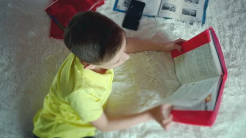Little boy does homework, reads a book in bed. books are scattered on the bed. Stock Footage 132059165