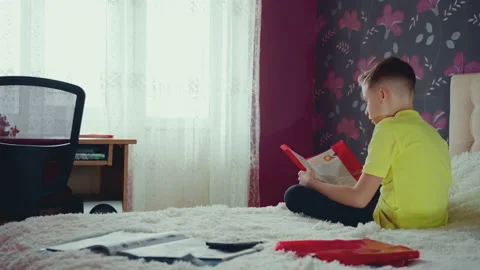 Little boy does homework, reads a book in bed. books are scattered on the bed. Stock Footage 132059571