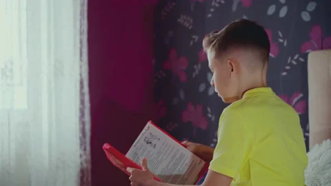 Little boy does homework, reads a book in bed. books are scattered on the bed. Stock Footage 132059954