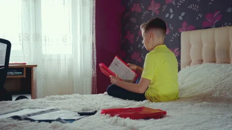 Little boy does homework, reads a book in bed. books are scattered on the bed. Stock Footage 132060199