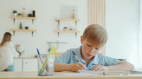 Little boy is doing homework at home sitting at the table, writing in notebook Video stock 195260905