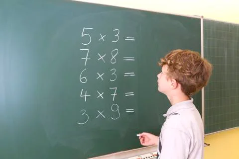 Little boy is doing some maths at a blackboard in school 库存照片