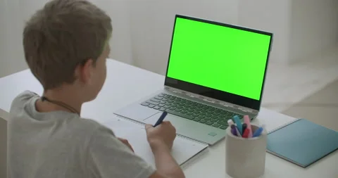 Little boy is drawing sitting at table with laptop with green screen for chroma Stock Footage 138864850