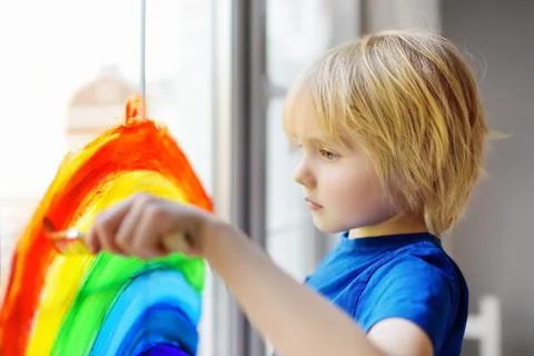 Little boy drawing on window rainbow while coronavirus quarantine. Rainbow si Foto stock