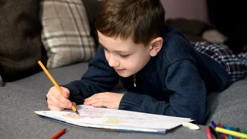 Little boy draws in coloring with colored pencils on sofa at home Stock Footage 170262907
